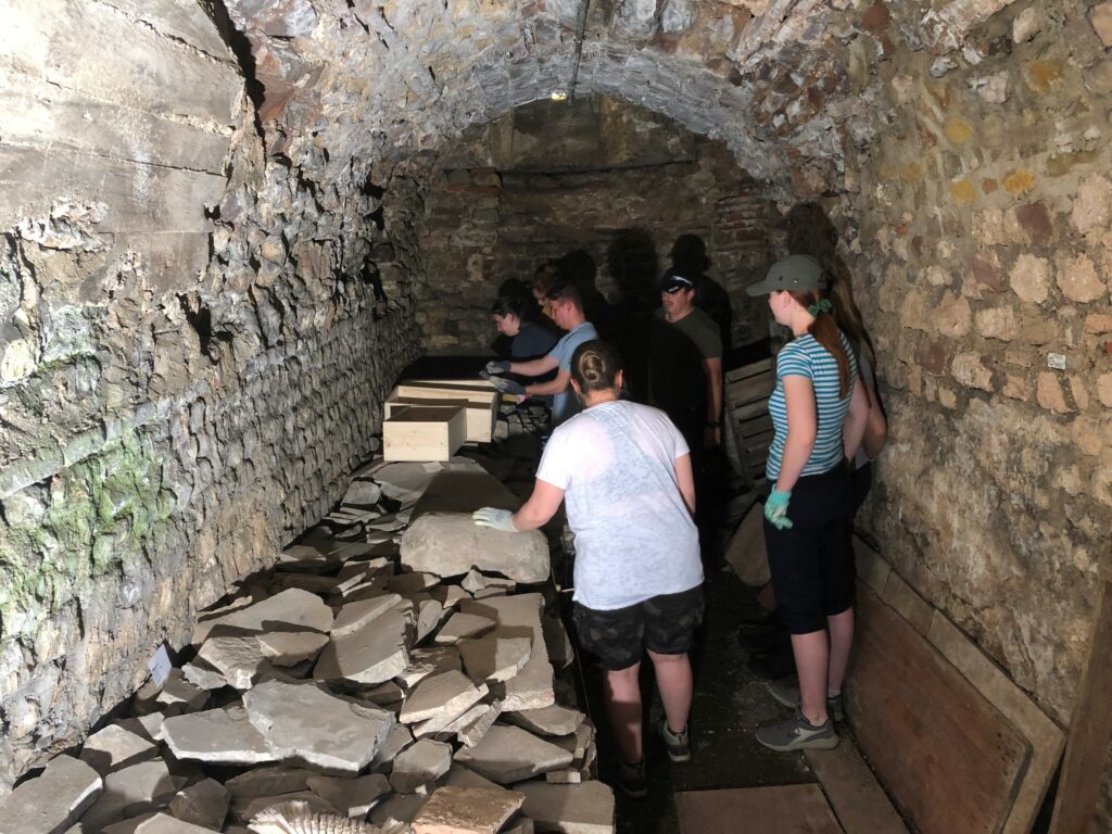 In einem Gewölbe steht die Gruppe Bochumer Archäolog:innen neben den zu bearbeitenden Marmorfragmenten.