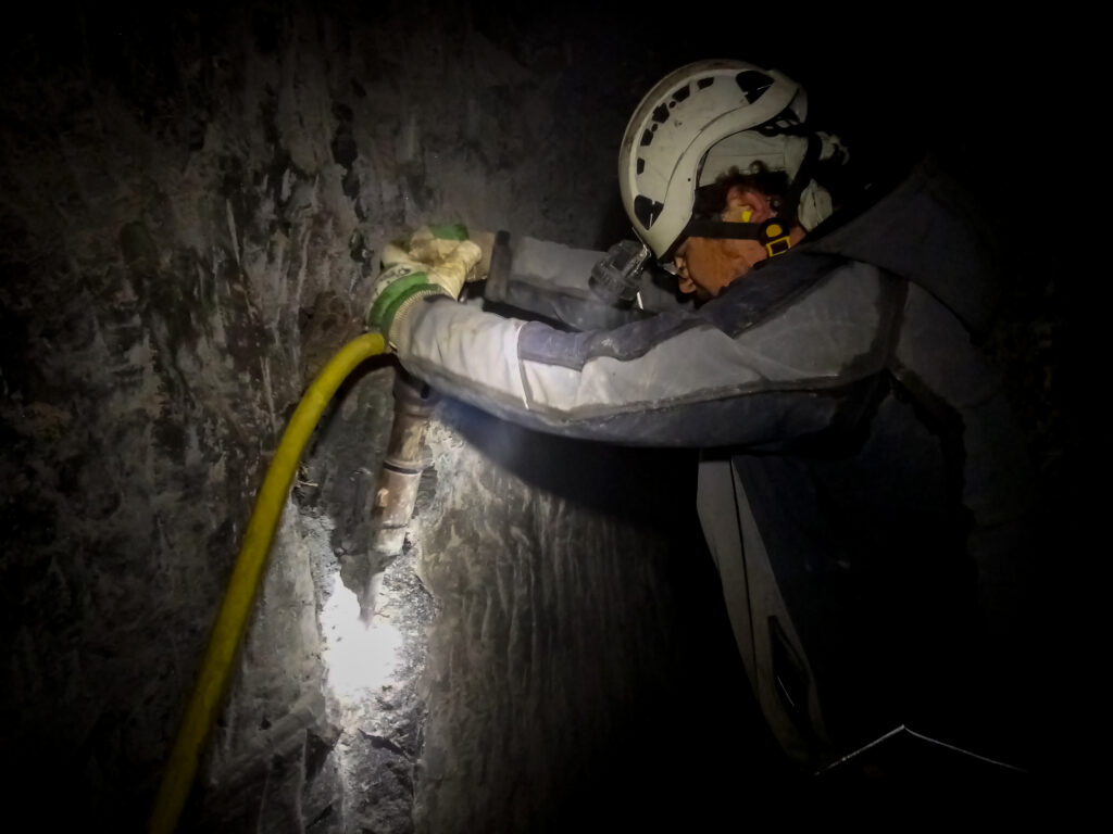 Im Schein seiner Helmlampe macht ein Mann mithilfe eines Presslufthammers Vortrieb in einem Bergwerksstollen.